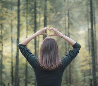 Frau formt ein Herz mit ihren Händen im Wald